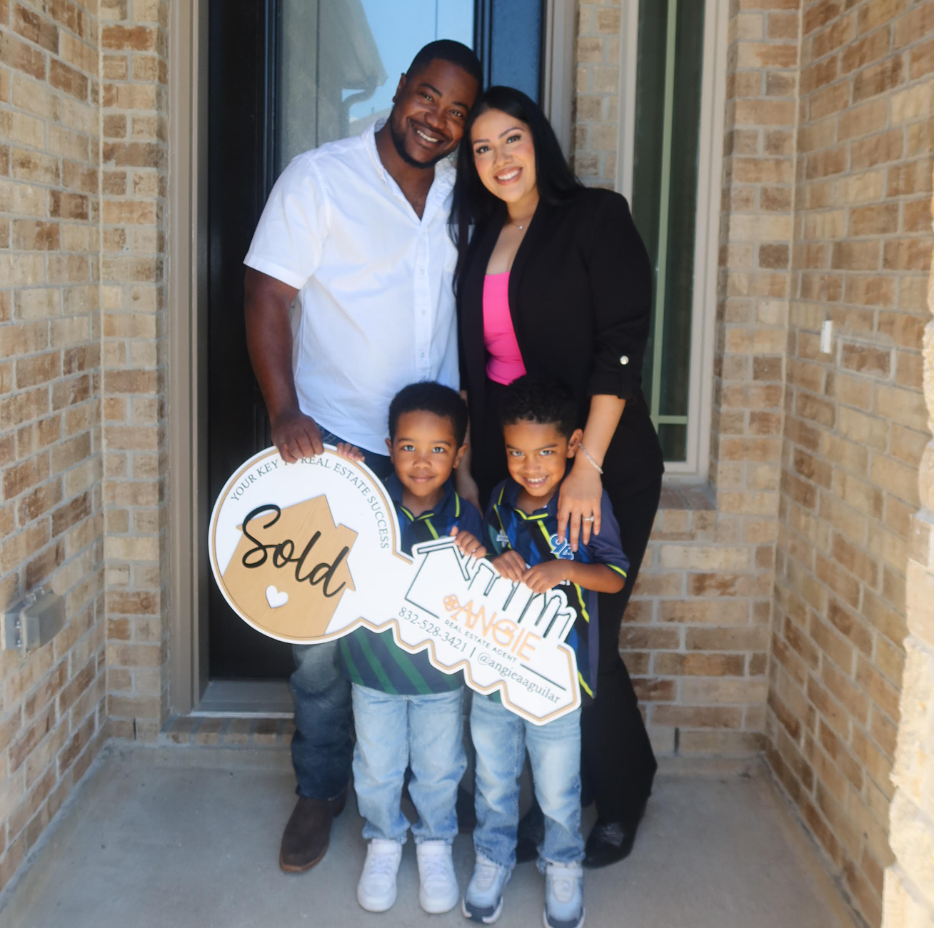 Family holding a Sold key at their new brick home