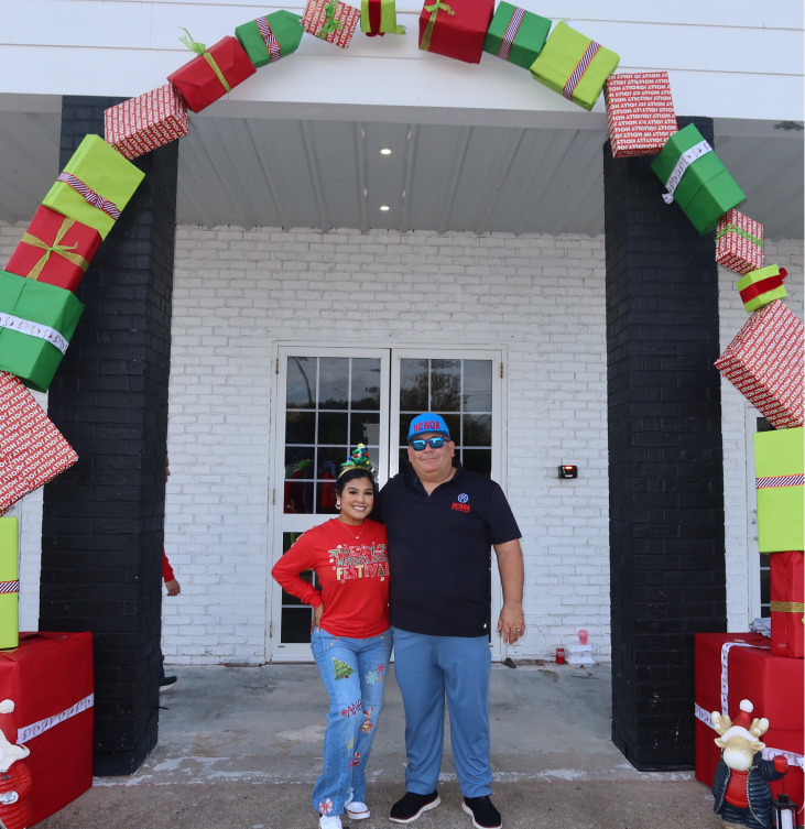 Angie Aguilar and a volunteer under a holiday gift archway